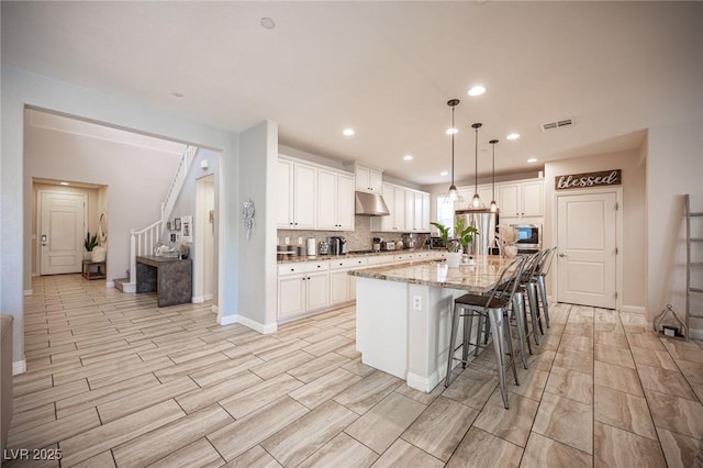 2198 Maderno St, Henderson, NV 89044 - kitchen with under cabinet range hood, white cabinetry, light stone countertops, and a breakfast bar