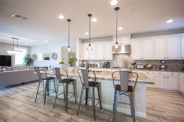 2198 Maderno St, Henderson, NV 89044 - kitchen with visible vents, decorative backsplash, light stone countertops, white cabinetry, and under cabinet range hood