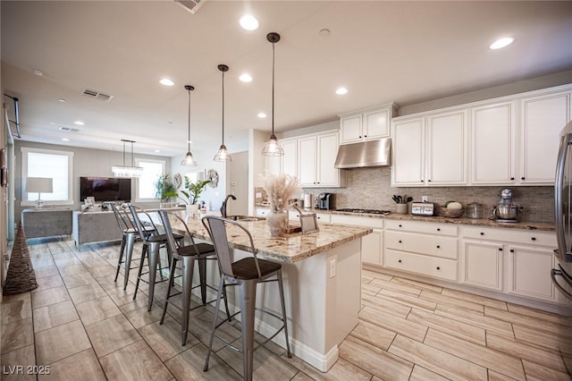 2198 Maderno St, Henderson, NV 89044 - kitchen featuring decorative backsplash, visible vents, light stone countertops, under cabinet range hood, and white cabinetry