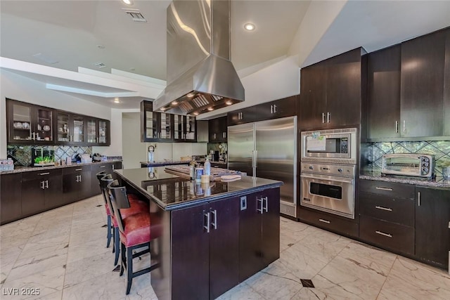 72 Innisbrook Ave, Las Vegas, NV 89113 - kitchen with built in appliances, island range hood, light marble finish floors, tasteful backsplash, and glass insert cabinets