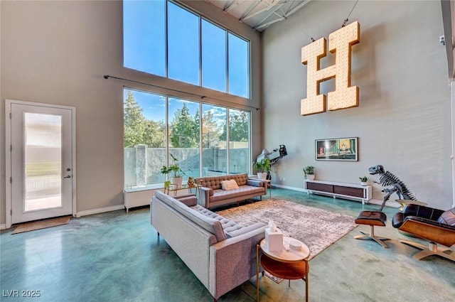 living room with a high ceiling, concrete floors, baseboards, and plenty of natural light