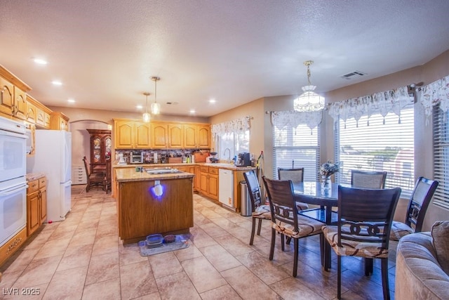 5180 N Dapple Gray Rd, Las Vegas, NV 89149 - kitchen featuring a kitchen island, white appliances, a chandelier, arched walkways, and decorative light fixtures