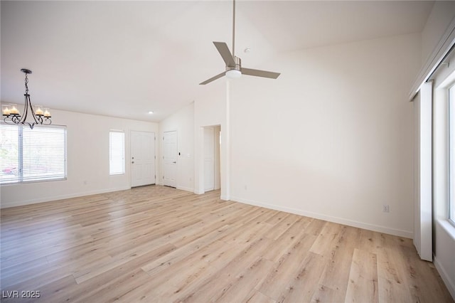 unfurnished living room with light wood-style floors, baseboards, ceiling fan with notable chandelier, and vaulted ceiling