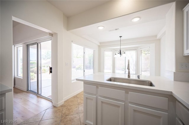 kitchen with an inviting chandelier, a peninsula, light countertops, a sink, and decorative light fixtures