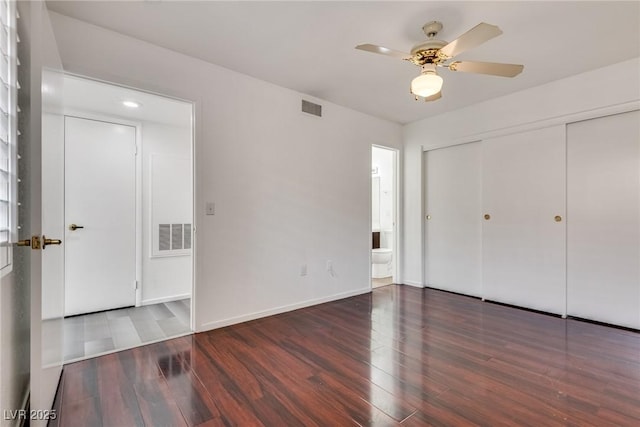 unfurnished bedroom featuring ensuite bathroom, a closet, wood finished floors, and visible vents