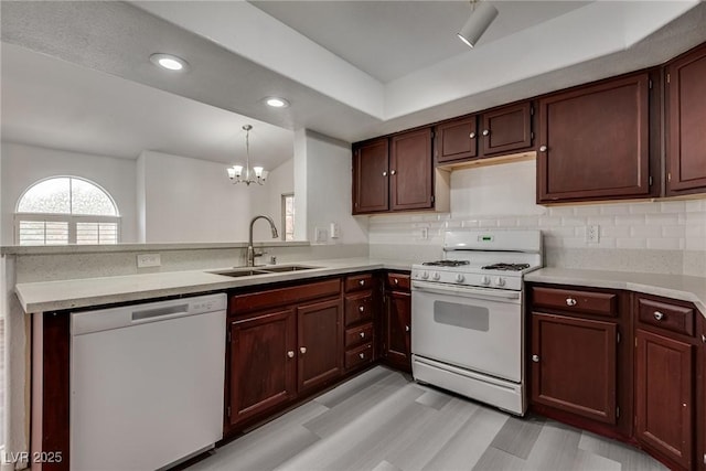 kitchen featuring a sink, white appliances, light countertops, a chandelier, and a peninsula