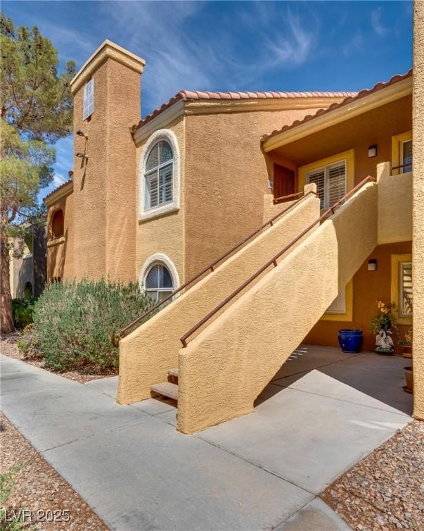 view of home's exterior with stucco siding, a chimney, and a tiled roof