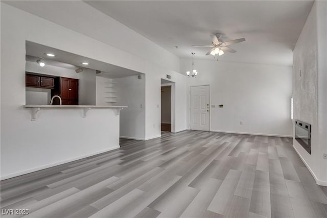 unfurnished living room with light wood-style floors, heating unit, ceiling fan with notable chandelier, and baseboards