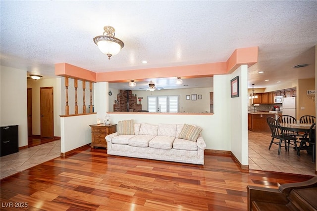 living room featuring a textured ceiling, baseboards, a ceiling fan, and light wood-style flooring