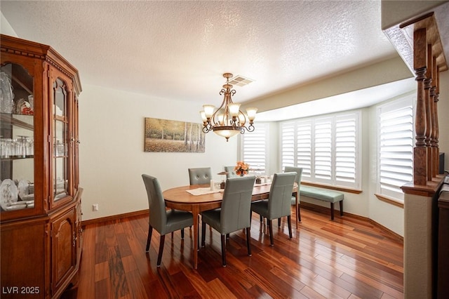 dining room with dark wood-style flooring, a textured ceiling, a chandelier, baseboards, and visible vents