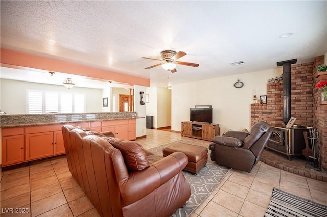 living room with a ceiling fan, a wood stove, light tile patterned flooring, and visible vents
