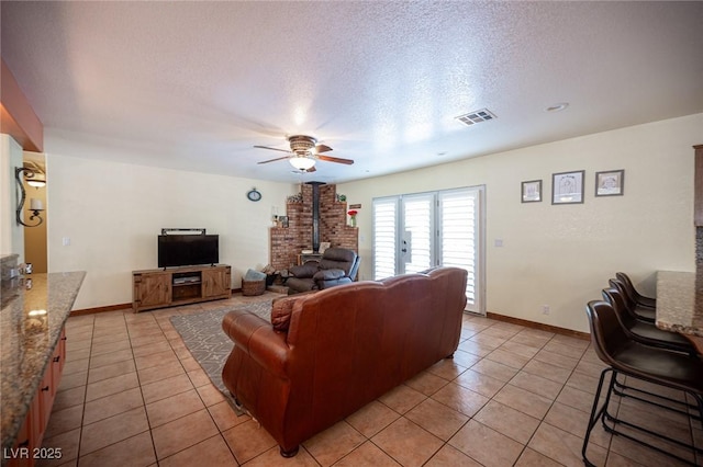 living room featuring light tile patterned floors, a wood stove, a textured ceiling, and visible vents