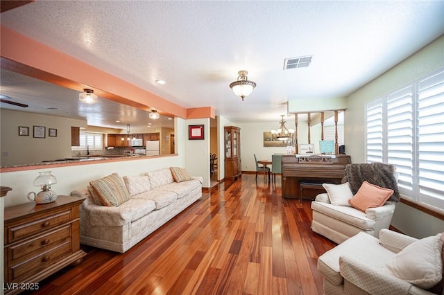 living area with visible vents, wood finished floors, baseboards, recessed lighting, and a notable chandelier