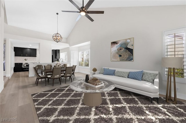6961 Emerald Springs Ln, Las Vegas, NV 89113 - living area featuring light wood finished floors, high vaulted ceiling, ceiling fan, baseboards, and a chandelier