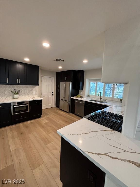 6961 Emerald Springs Ln, Las Vegas, NV 89113 - kitchen featuring stainless steel appliances, dark cabinets, a sink, light stone countertops, and backsplash