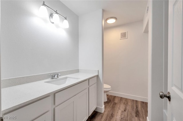 bathroom featuring vanity, baseboards, wood finished floors, and toilet