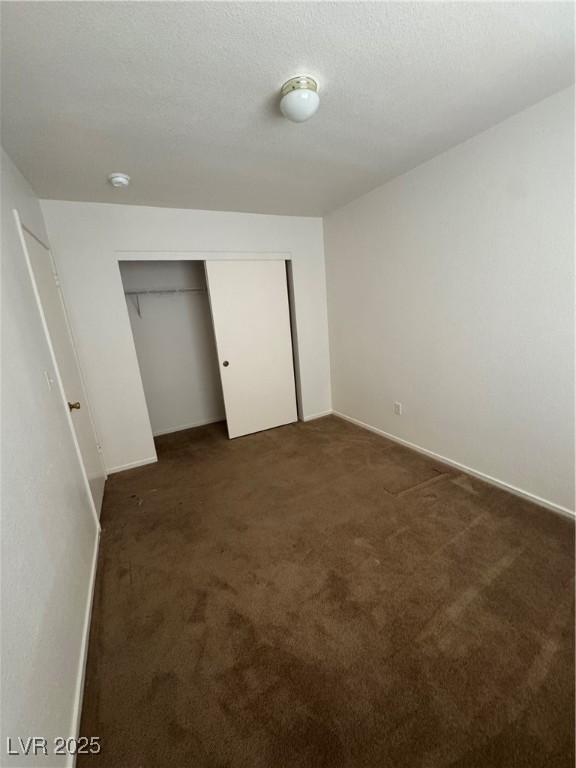 unfurnished bedroom with baseboards, a closet, and dark colored carpet