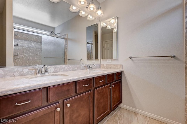 full bath featuring double vanity, baseboards, walk in shower, and a sink