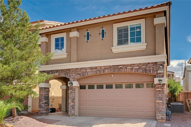 mediterranean / spanish-style home featuring decorative driveway, a garage, stucco siding, and stone siding