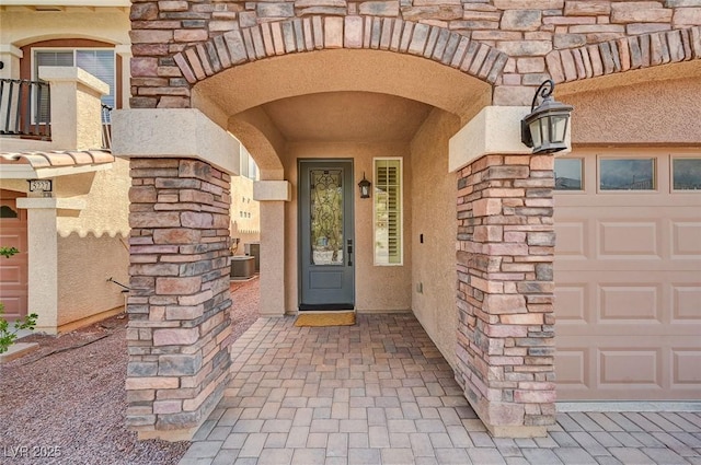 property entrance featuring central AC, a garage, stucco siding, and stone siding