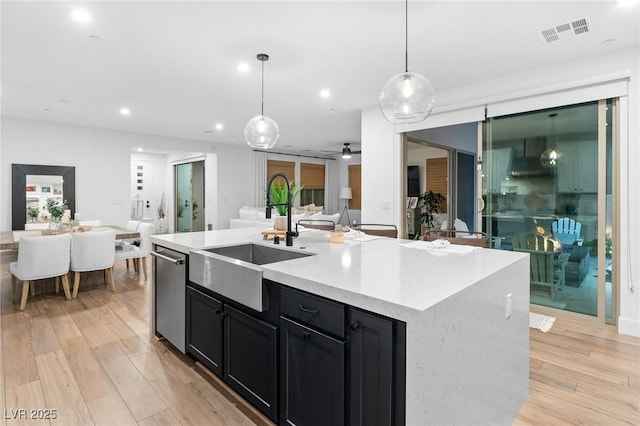 kitchen with visible vents, stainless steel dishwasher, a sink, open floor plan, and dark cabinets