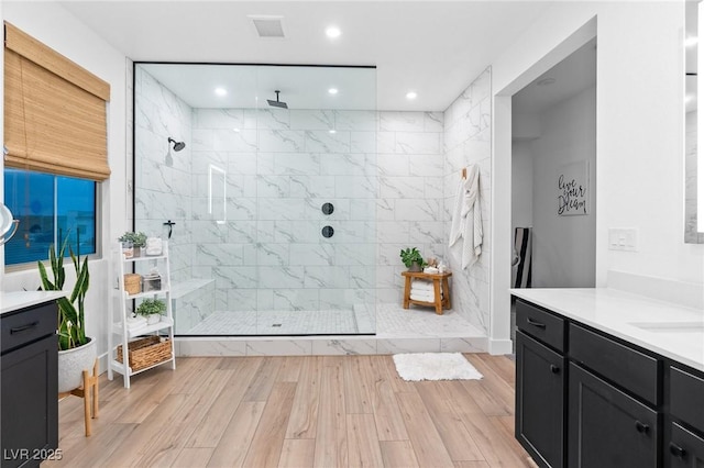 bathroom with a walk in shower, visible vents, wood finished floors, and vanity