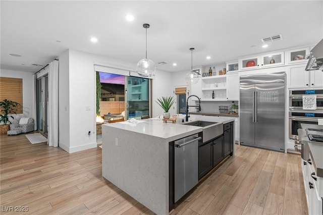 kitchen with appliances with stainless steel finishes, white cabinetry, a sink, light countertops, and light wood-style flooring