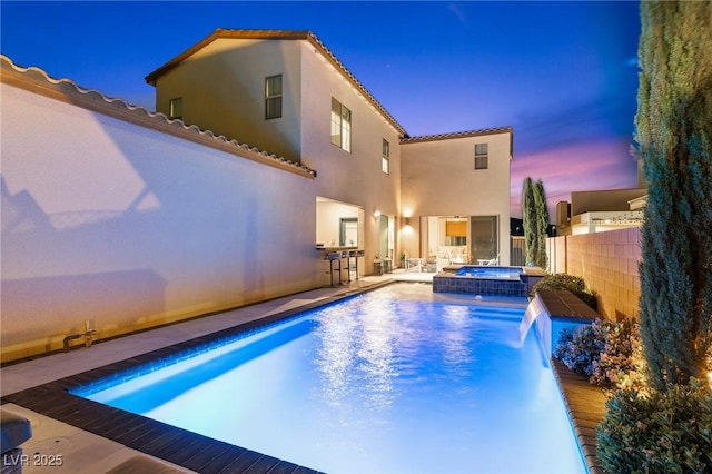pool at dusk featuring a patio area, a pool with connected hot tub, and fence