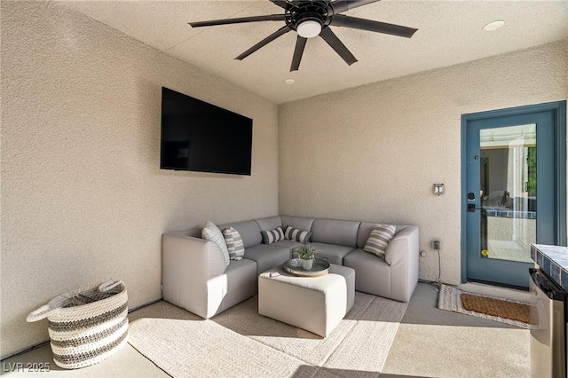 carpeted living area with a textured wall and a ceiling fan