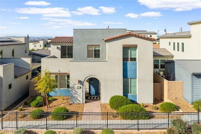 mediterranean / spanish home featuring a tiled roof, fence, and stucco siding