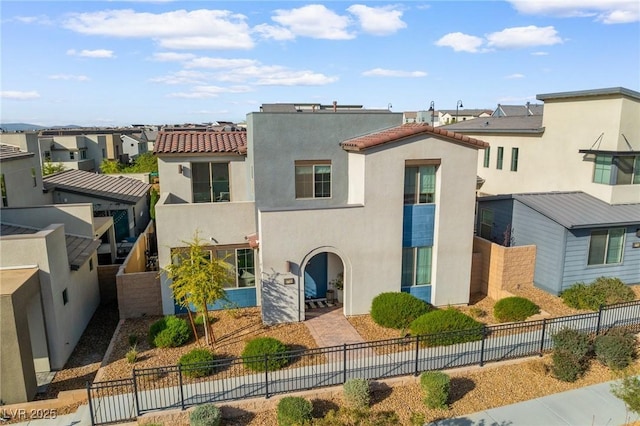 mediterranean / spanish-style house featuring a residential view, stucco siding, a fenced backyard, and a tile roof