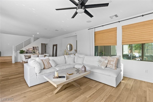 living room featuring visible vents, stairs, wood finished floors, baseboards, and ceiling fan