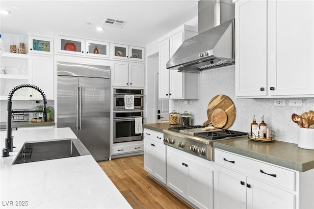 kitchen with decorative backsplash, wall chimney exhaust hood, white cabinetry, a sink, and stainless steel appliances