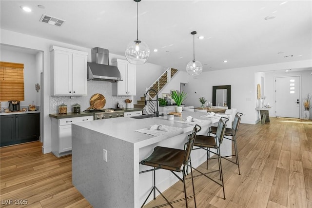 kitchen featuring visible vents, wall chimney exhaust hood, light wood-style floors, and white cabinetry