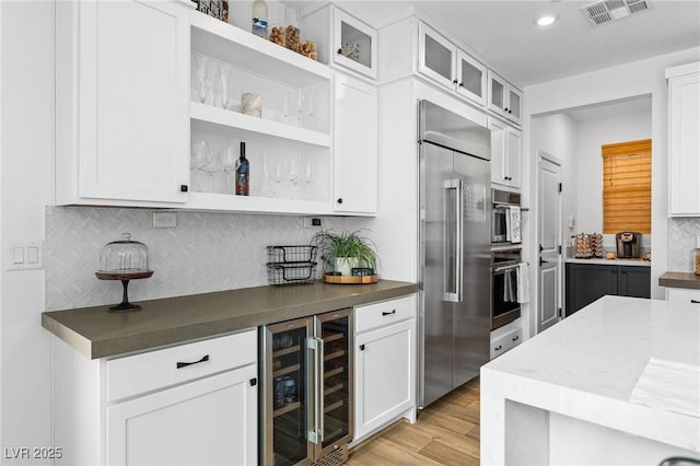 kitchen featuring backsplash, visible vents, built in refrigerator, beverage cooler, and white cabinetry
