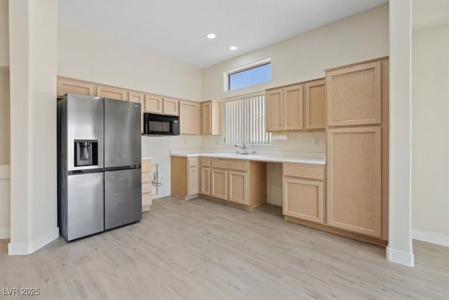 kitchen with light brown cabinetry, black microwave, stainless steel fridge, and light wood-type flooring