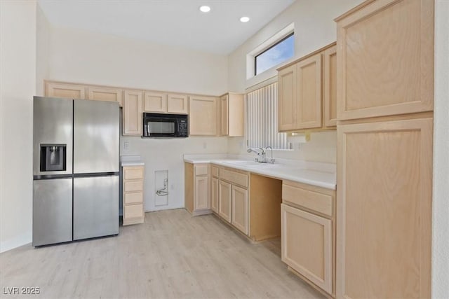 kitchen with light brown cabinets, black microwave, stainless steel fridge, a sink, and light wood finished floors