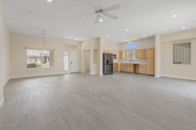 unfurnished living room with baseboards, recessed lighting, light wood-style flooring, and ceiling fan with notable chandelier