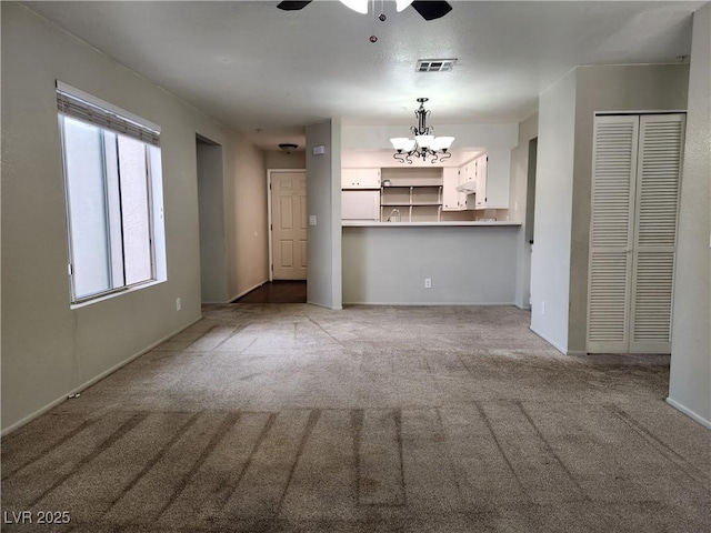 unfurnished living room with baseboards, visible vents, light carpet, and ceiling fan with notable chandelier