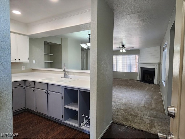 kitchen with gray cabinetry, a sink, ceiling fan with notable chandelier, and dark wood-type flooring