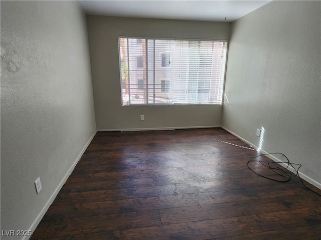 unfurnished room with wood-type flooring, a textured wall, and baseboards