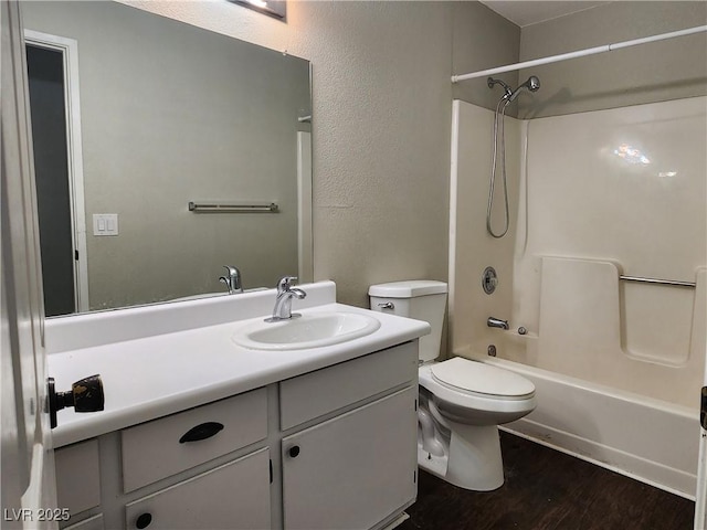 bathroom featuring wood finished floors, vanity, toilet,  shower combination, and a textured wall