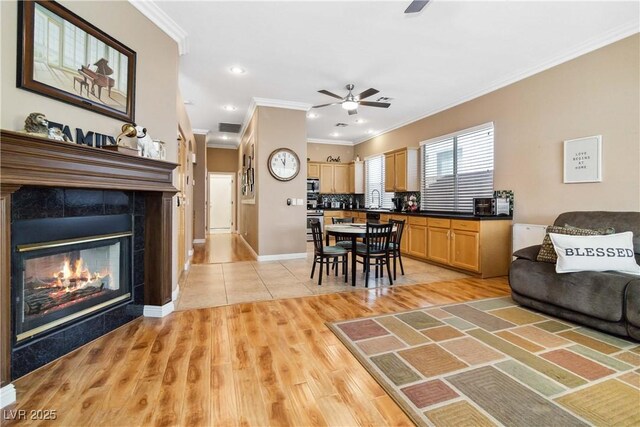 living room with a ceiling fan, light wood-style flooring, ornamental molding, visible vents, and a tile fireplace