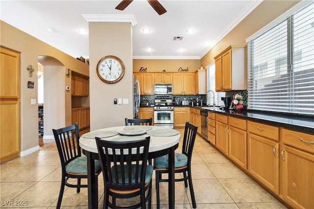 kitchen featuring ceiling fan, light tile patterned flooring, arched walkways, stainless steel appliances, and tasteful backsplash