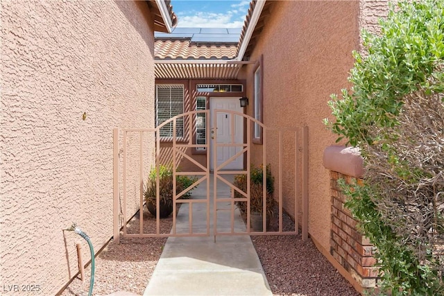 property entrance featuring roof mounted solar panels, stucco siding, and a gate