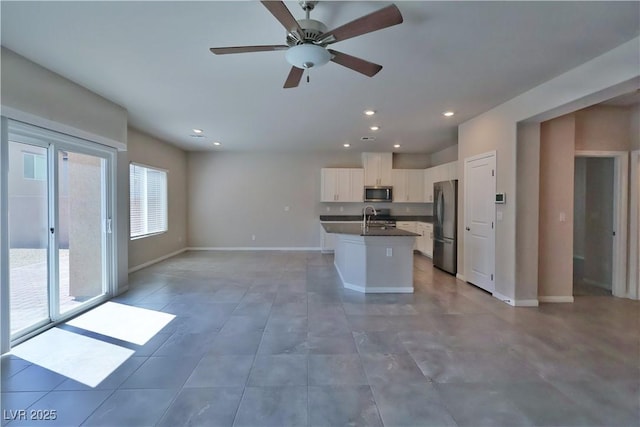 kitchen with dark countertops, open floor plan, white cabinets, a sink, and stainless steel appliances