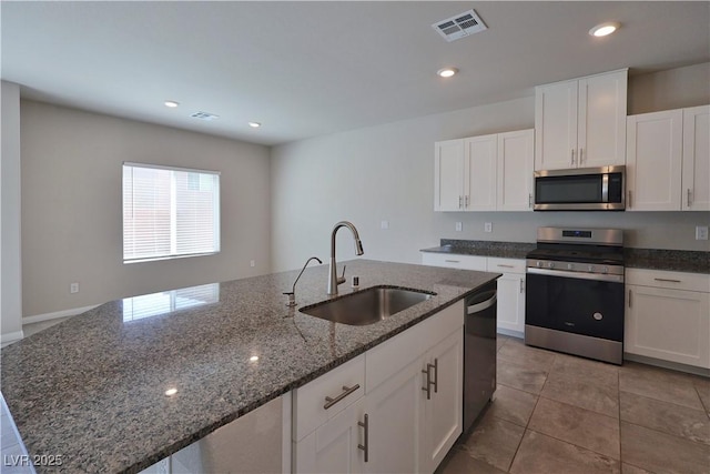 kitchen with visible vents, an island with sink, white cabinets, a sink, and appliances with stainless steel finishes