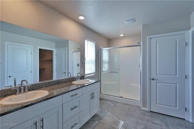 full bathroom with double vanity, a sink, visible vents, and a shower stall