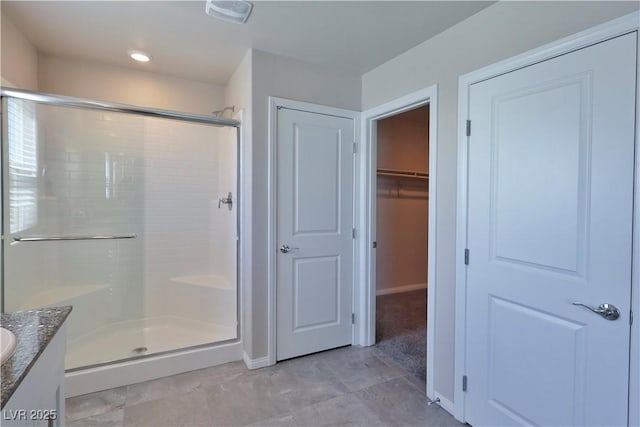 bathroom featuring a walk in closet, visible vents, a shower stall, vanity, and baseboards
