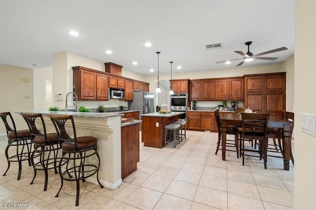 6335 Iginlas Goal Ave, Las Vegas, NV 89131 - kitchen with visible vents, a peninsula, a breakfast bar, appliances with stainless steel finishes, and light tile patterned floors